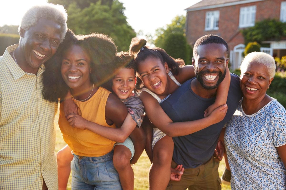 Three generations of a smiling family hug outdoors on a sunny day