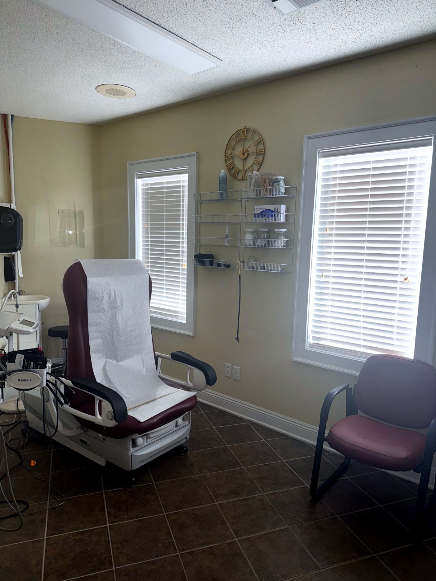 A patient room at BAZ Family Medical Clinic with an exam chair, supply shelves and two windows